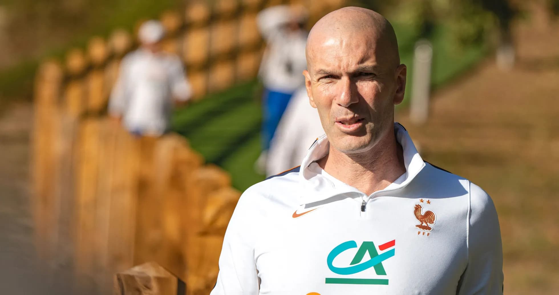 Coach walking near training ground with players in background