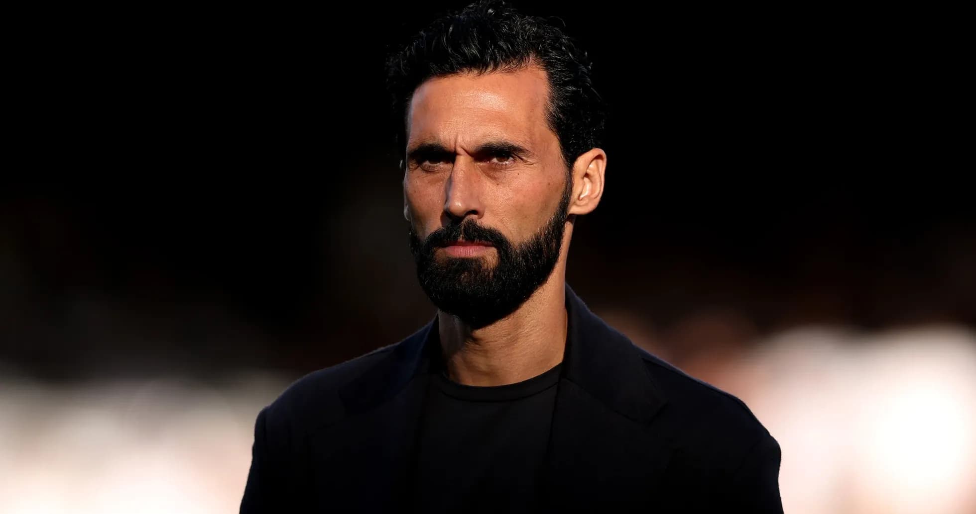 Man with beard and dark attire looking serious