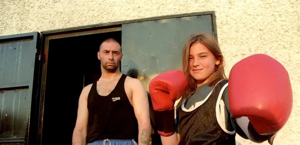 Young female boxer posing with trainer outside gym