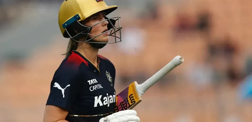 Cricketer in helmet walking with bat on field