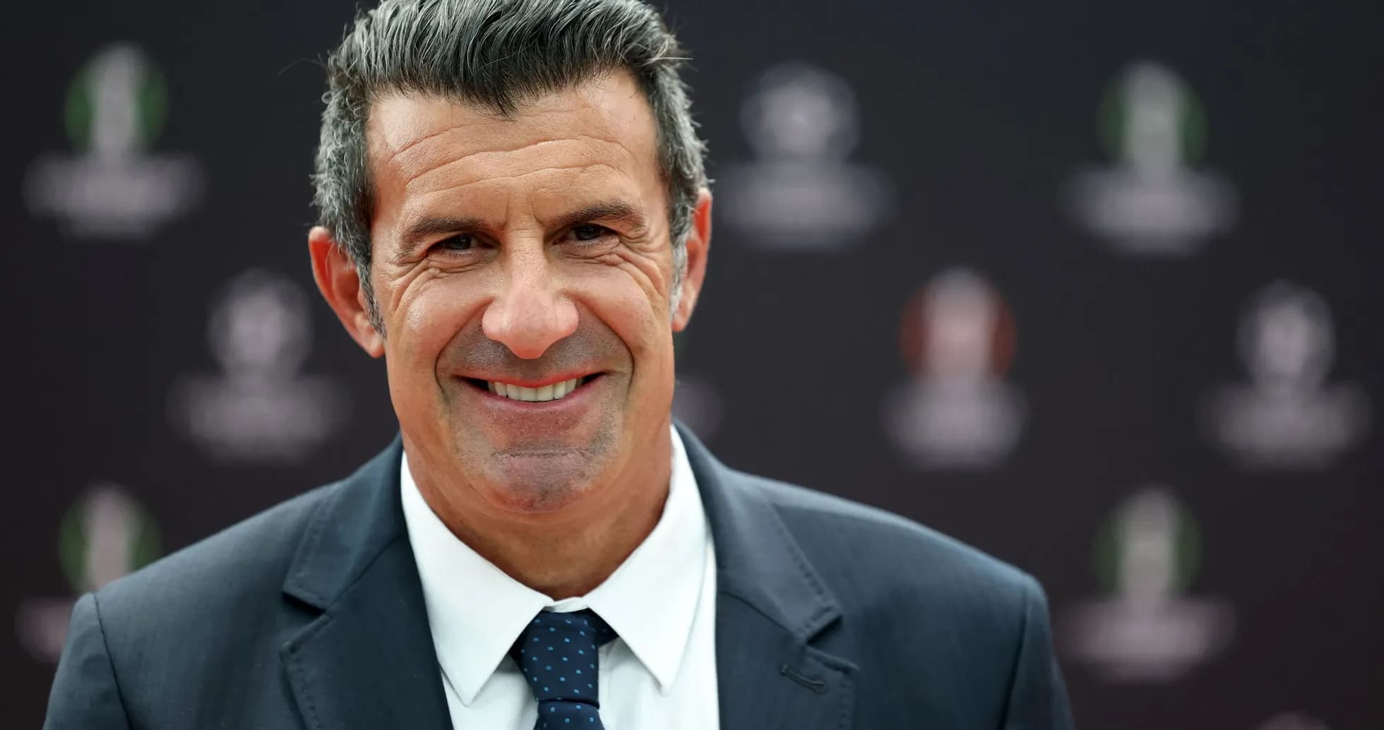 Man in suit smiling at press event backdrop