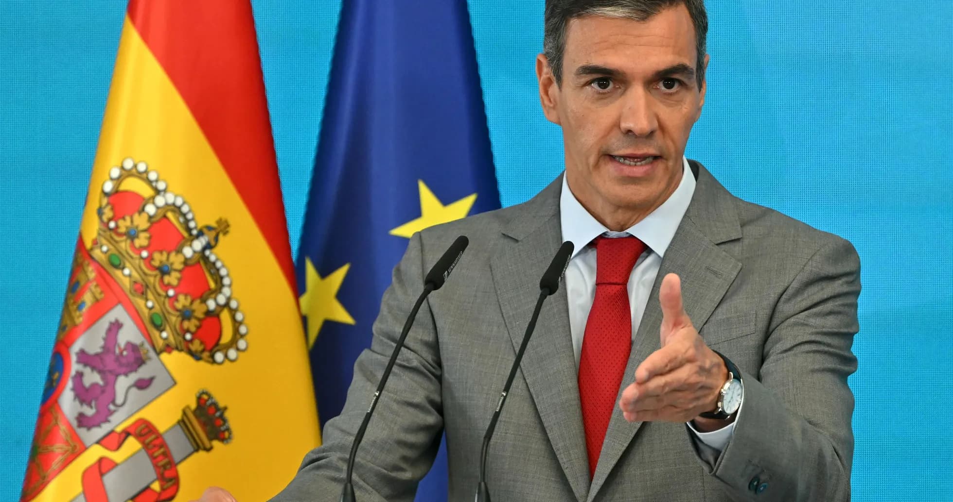 Politician speaking at a podium with flags behind