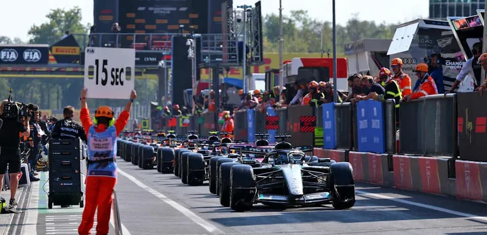 Race cars lined up in pit lane with time penalty sign