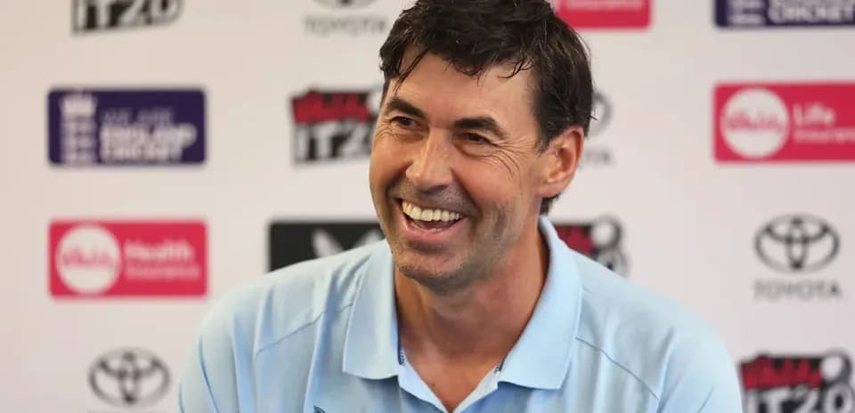 Cricket coach smiling at press conference backdrop