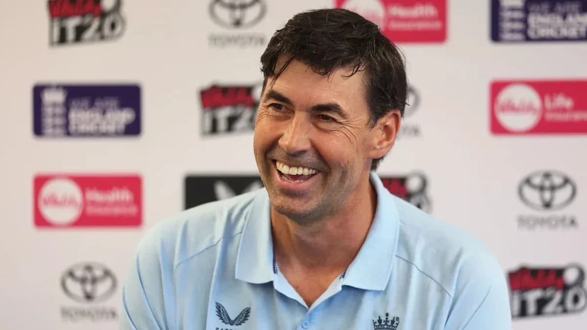 Cricket coach smiling at press conference backdrop