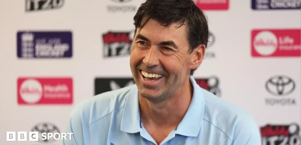 Cricket coach smiling at press conference podium