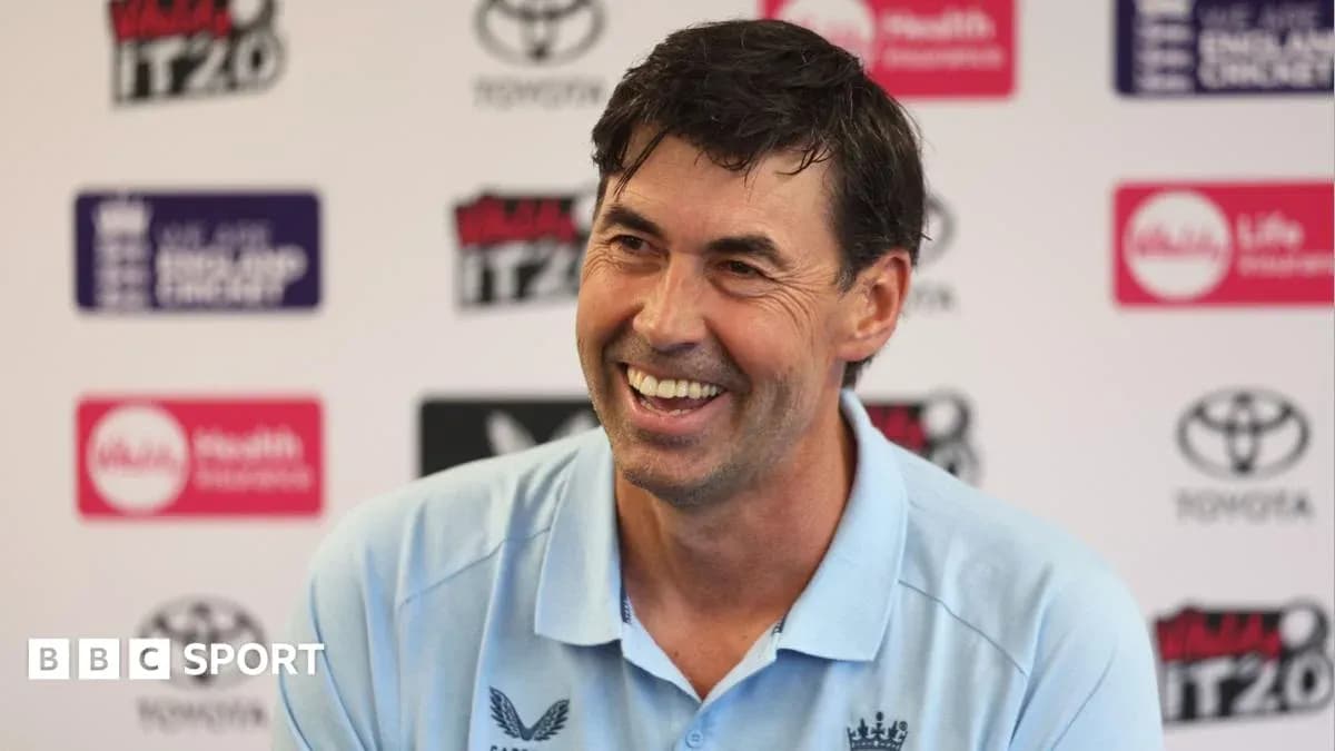 Cricket coach smiling at press conference podium