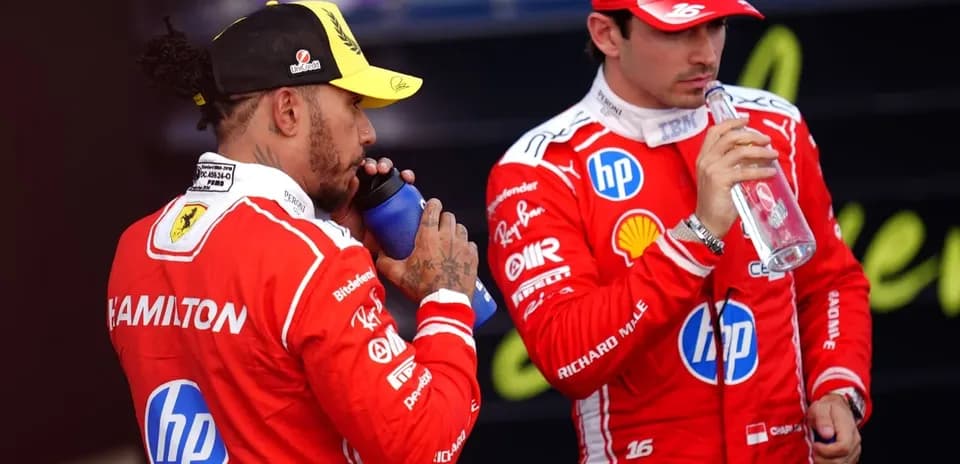Two drivers in red suits drinking water bottles