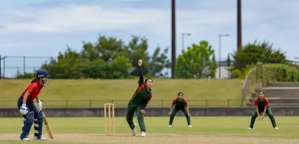 Bowler delivering ball with fielders positioned nearby
