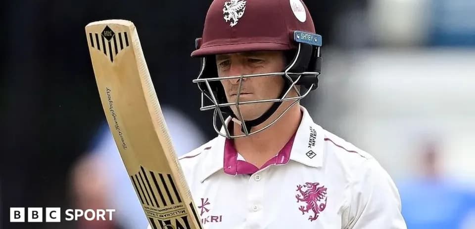 Cricketer holding bat, wearing helmet and uniform