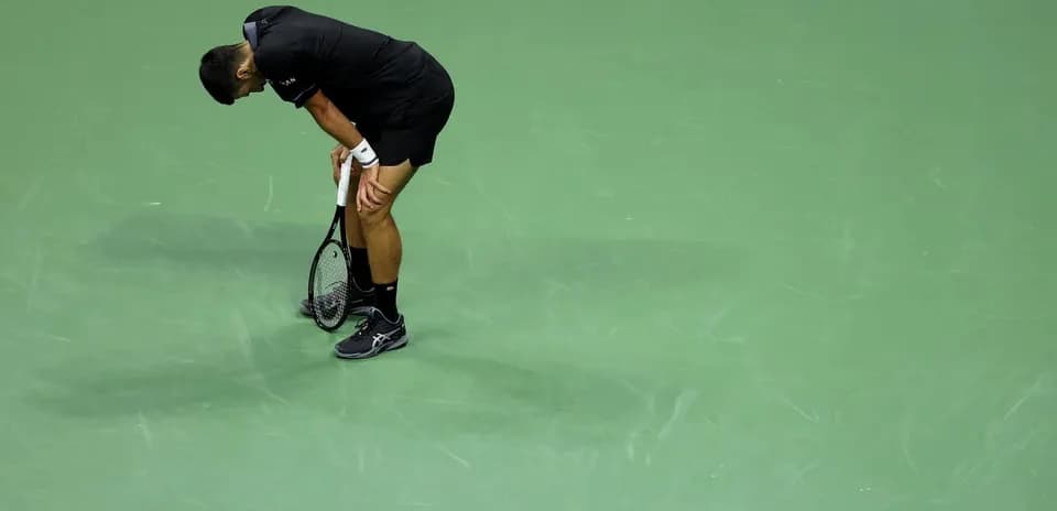 Tennis player bending over on court with racket