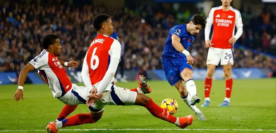Chelsea player shooting while Arsenal defenders tackle