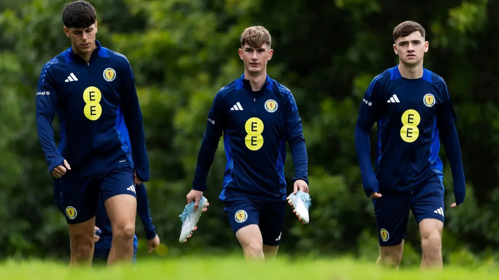 Three players walking in training gear on pitch Three players walking in training gear on pitch